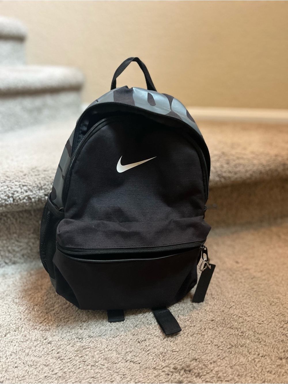 Mini Nike Black Backpack with White Swoosh and Gray Pattern with side pockets.